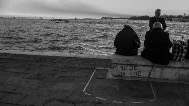 Venice, people sitting close to the lagoon.